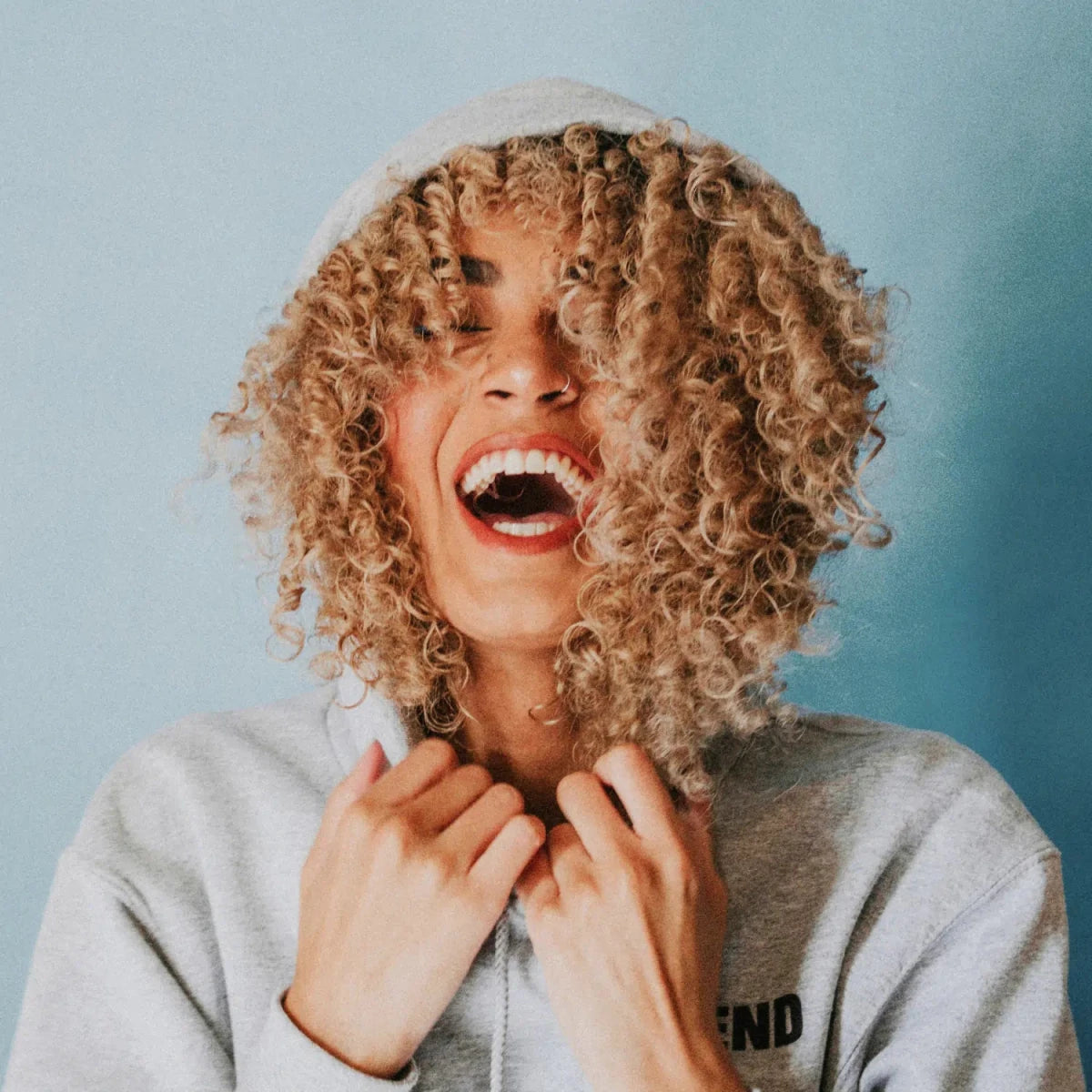 Biotin und Haarvitamine: Lachende Frau, volle Locken unter Kaputze