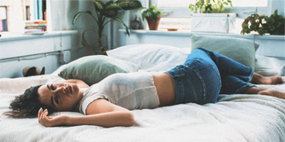 Eine Frau liegt auf einem Bett mit natürlichen Elementen im Hintergrund.